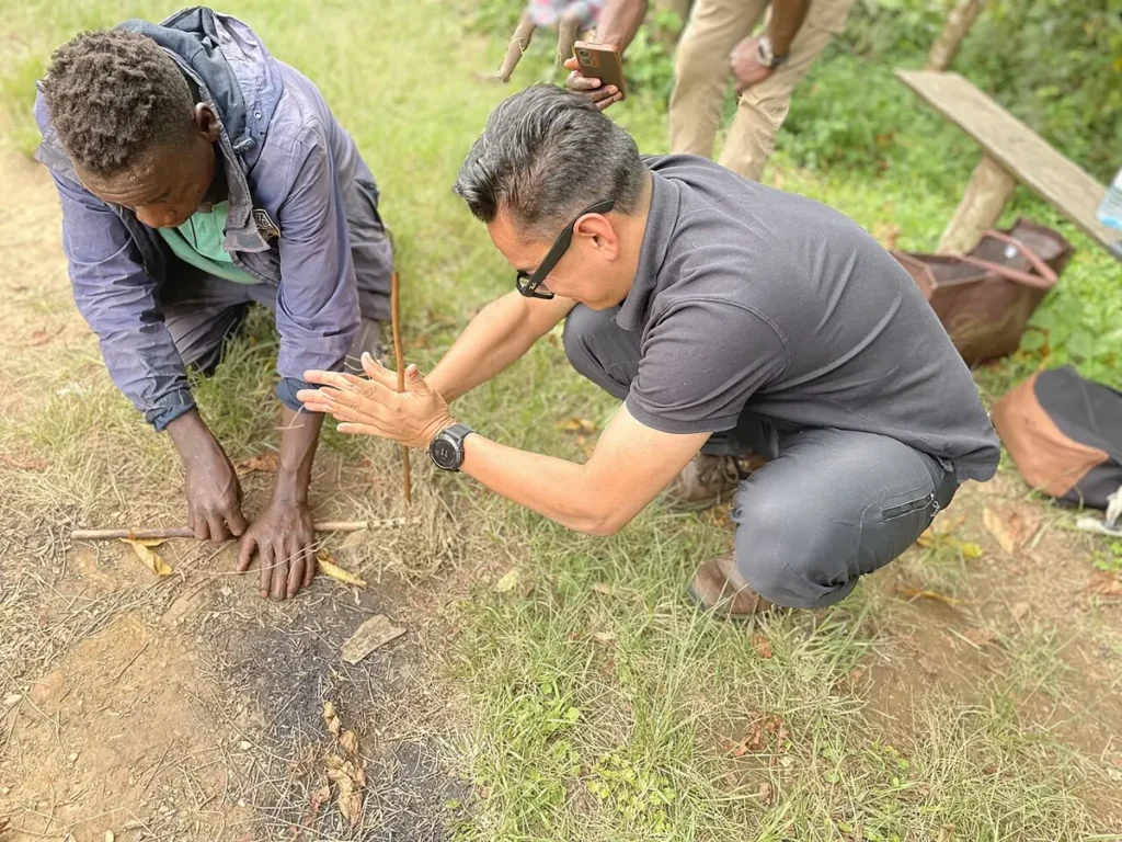 Batwa guide showing a visitor how to make fire by hand