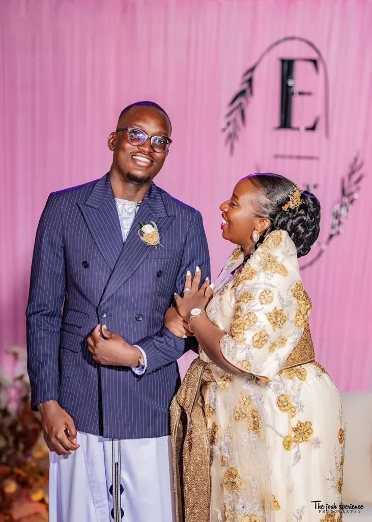 Man in a white kanzu and jacket beside a woman in a gomesi
